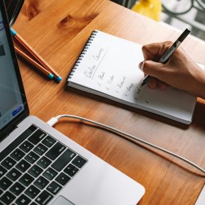 A person writing notes while researching online courses on a laptop in a home setting.